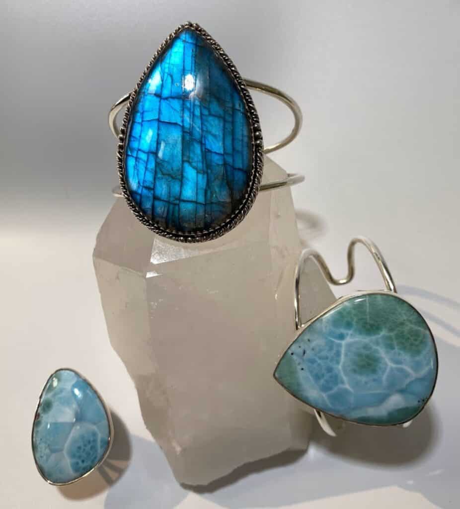 jewelry on a white quartz crystal. A teardrop blue Larimar cuff bracelet, a teardrop labradorite cuff bracelet, and a freeform larimar ring