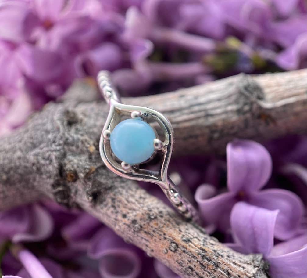 a small circular blue chalcedony and sterling silver ring laid on a branch against lilac flowers